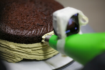 pastry chef designer using pistachio cream filling piping bag on layered dark chocolate cake at...