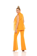 Middle aged smiling senior woman in yellow sleevless jacket and trousers posing on a white background. Side view.