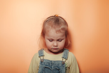 Portrait (face) of sorrowful blonde little girl wear casual clothes at beige background, closed...