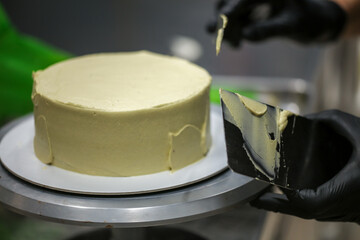 Decorator using spatula and scraper smoothing green pistachio buttercream frosted cake