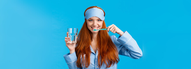 Enthusiastic upbeat, lively redhead woman, foxy girl with pretty smile, brushing teeth holding toothbrush and glass water, wake up morning, getting dressed, wearing sleep mask and pyjama