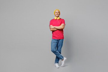 Full body cheerful fun smiling young man of African American ethnicity 20s he wears pink t-shirt yellow hat headphones hold hands crossed folded look camera isolated on plain grey background studio.