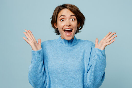 Young Surprised Overjoyed Fun Winner Caucasian Woman Wear Knitted Sweater Look Camera Spread Hands Say Wow Isolated On Plain Pastel Light Blue Cyan Background Studio Portrait People Lifestyle Concept