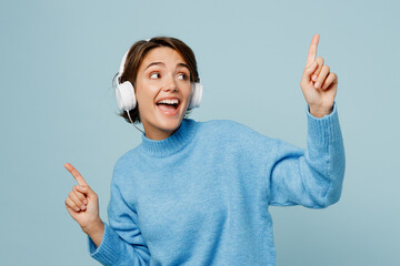 Young cheerful fun happy caucasian woman wear knitted sweater headphones listen to music raise up...
