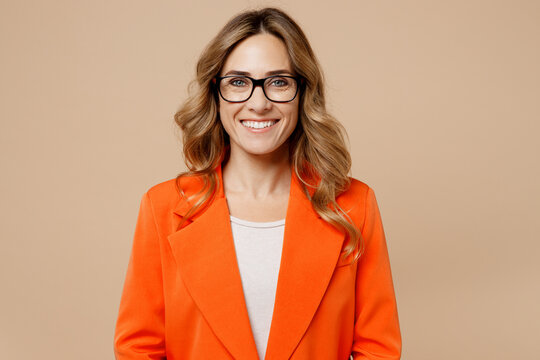 Close up young fun happy successful employee business woman corporate lawyer 30s wearing classic formal orange suit glasses work in office look camera isolated on plain beige color background studio.