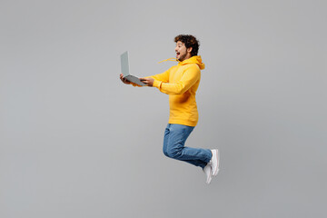 Full body side view young Indian IT man 20s he wearing casual yellow hoody jump high hold use work...