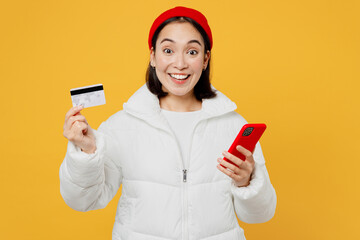 Young surprised woman of Asian ethnicity wear white padded windbreaker jacket red hat using mobile...