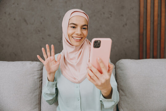 Young muslim woman in hijab casual clothes doing selfie shot on mobile cell phone sits on sofa couch stay at home flat rest relax spend free spare time in living room indoor People uae islam concept