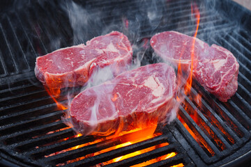 Barbecue dry aged angus rib-eye beef steak grilled as close-up on a charcoal grill with fire and...