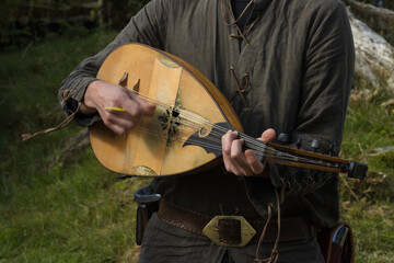 Man dressed in a garb playing a mediveal string instrument called Lute.