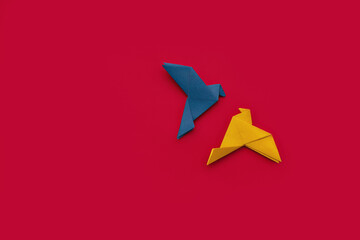 two doves made of origami paper in yellow and blue, in colors of Ukrainian flag on red background