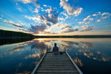Hiker Sitting on Dock at Calm Lake at Sunset, Saskatchewan, Canada