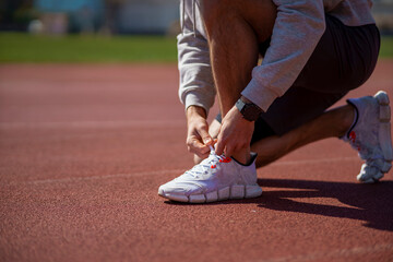 Runner man tying shoelace in the stadium, cross training workout. Sporty male training outside