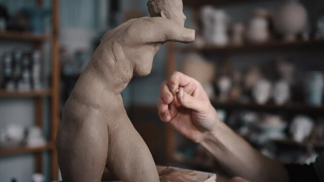 Close-up of male sculptor creates a bust and puts his hands clay on the skeleton of the sculpture.