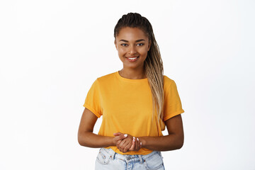 Image of smiling Black woman holding hands together and looking at camera helpful, assisting customer or client, standing friendly against white background - 555523858