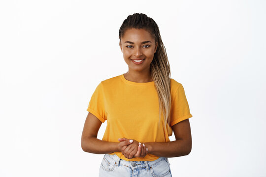 Image of smiling Black woman holding hands together and looking at camera helpful, assisting customer or client, standing friendly against white background