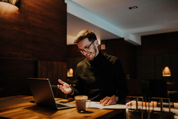 Young businessman using laptop for online meeting while sitting in modern cafe