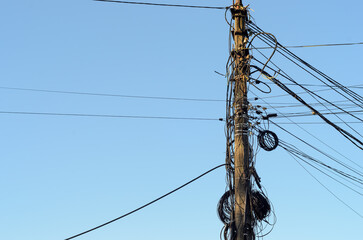 A concrete electric pole with numerous wires and coils on it  against the blue sky
