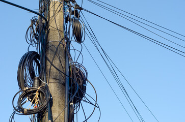 A concrete electric pole with numerous wires and coils on it  against the blue sky