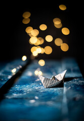 Fototapeta na wymiar close-up of an origami boat on a dark blue wooden background with bokeh light.artistic concept.