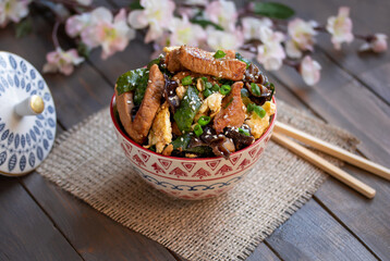 Moo shu pork. Bowl of homemade Chinese stir fry dish made with marinated pork, cucumber, egg scramble, black wood ear mushrooms and scallion. Selective focus, horizontal, wooden table.