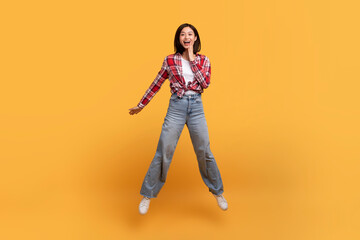 Wow. Full body length shot of surprised asian lady jumping, shocked by news or offer, yellow studio background