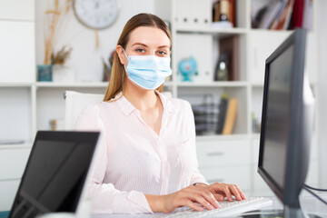 Young female worker wearing medical facial mask engaged in business activities in office