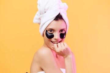 Horizontal photo, a woman with perfect skin on an orange background in a towel on her head and body with black patches on her face smiles relaxed