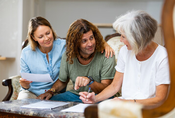 Obraz premium Positive couple and old woman talking about finances and taking notes, resting on the sofa at home