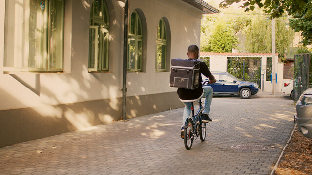 African american male courier delivering takeaway meal order, riding bike and carrying backpack with food. Delivery service worker giving fastfood to customers, restaurant express food.