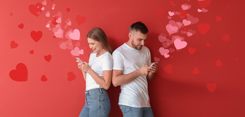 Portrait of young couple with mobile phones chatting online on red background. Valentine's Day...