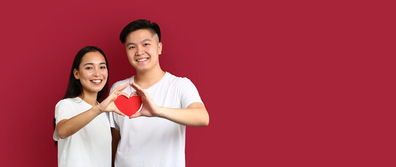 Happy young Asian couple holding paper heart on red background with space for text. Valentine's Day celebration