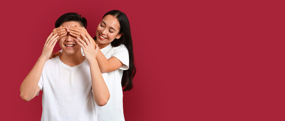 Portrait of happy young Asian couple on red background with space for text