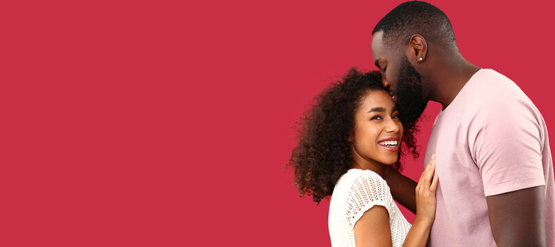 Portrait of happy African-American couple on red background with space for text