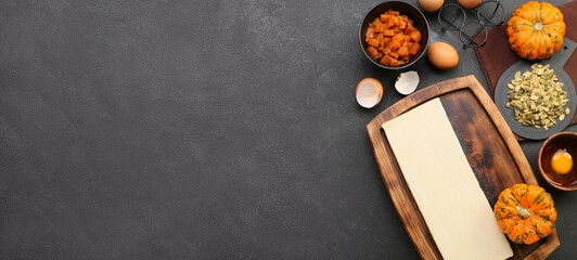 Raw dough and ingredients for preparing pumpkin pie on dark background with space for text