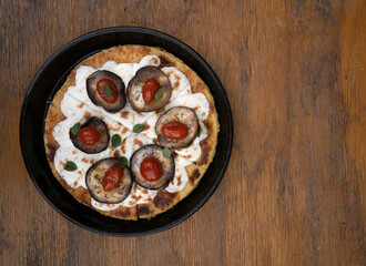 Vegan pizza. Top view of a vegetarian pizza with farinata, vegan mozzarella cheese, tomatoes, grilled eggplant and fresh oregano in a black pizza pan on the wooden table.