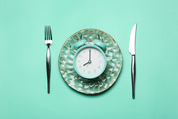 Alarm clock with plate and cutlery on blue background