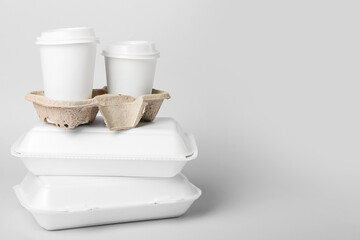 Stack of food boxes and holder with paper cups on light background