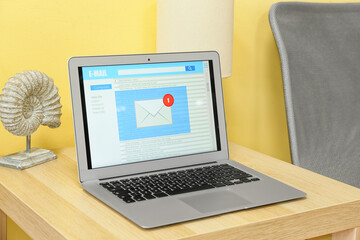 Modern laptop with opened e-mail box and decor on wooden table near color wall