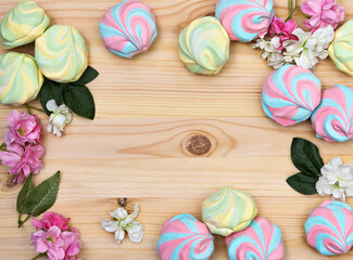 Frame made of colorful airy striped marshmallows and pink and white inflorescences on a light wooden background