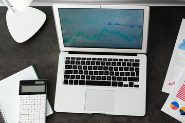 Laptop with stock data, calculator and notebook on table. Finance trading