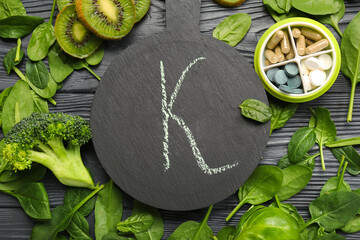 Board with letter k, container of pills and healthy products on black wooden background