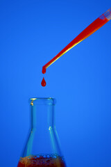 A drop of blood. Pipette. On a blue background. Medical flask with red liquid. Flask with blood. Dripping red liquid. A drop of red. Tests, blood group.