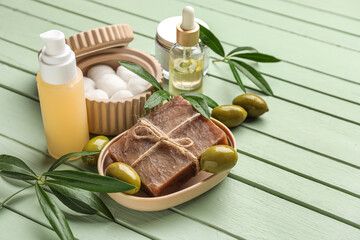 Natural cosmetics with olives, cotton balls and plant branches on green wooden background