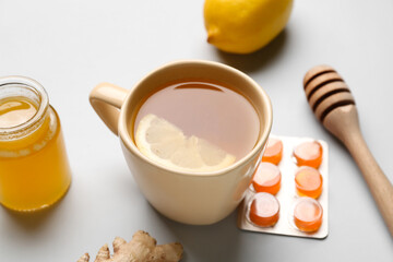 Cup of tea, pills for sore throat and honey on light background, closeup