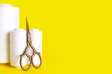 White thread spools and scissors on yellow background