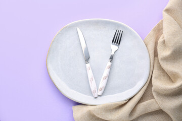 White plate with cutlery and napkin on lilac background