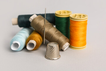 Thread spools, needle and thimble on grey background