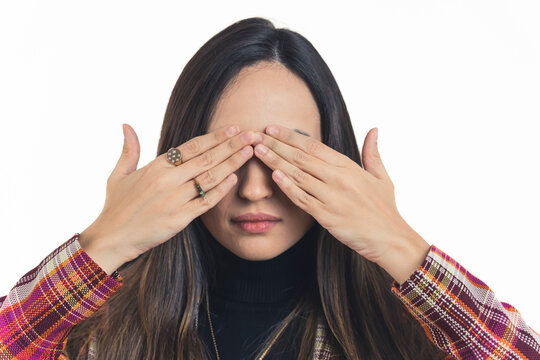 Latin american young adult woman with dark long hair facing camera covering her eyes with both hands and cold expression. White background copy space horizontal studio shot. High quality photo