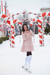 Happy joyful brunette holding Christmas caramel stick, standing the ice skates outside. Christmas...
